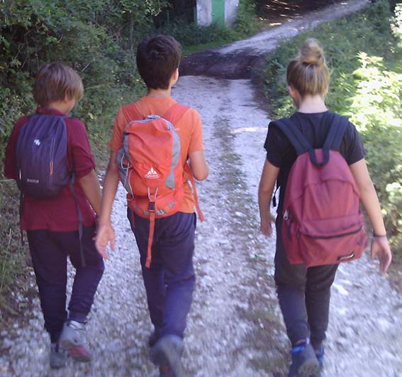 Tre bambini visti di spalle, zaino in spalla e passo spedito verso la vetta della montagna